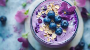 Close-up of a blueberry smoothie bowl garnished with oats, blueberries, and a purple edible flower