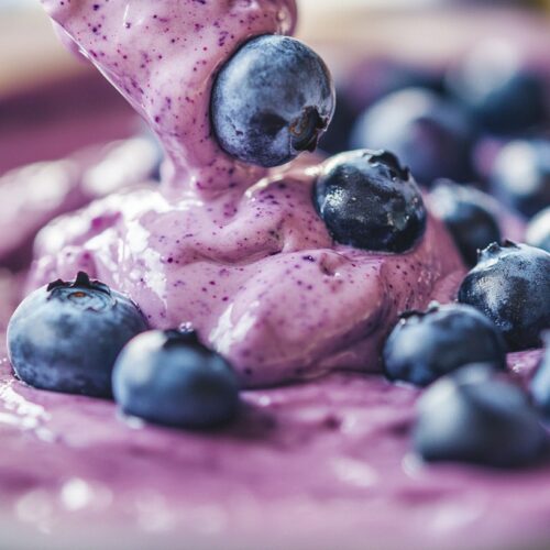 Close-up of blueberry cheesecake batter being poured, topped with fresh blueberries