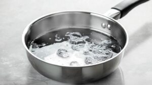 A stainless steel saucepan containing bubbling sugar syrup on a light surface