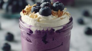 A jar of blueberry cheesecake with whipped cream, fresh blueberries, and a sprinkle of crumble on top