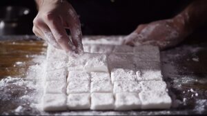 Hand cutting marshmallows into square pieces and coating them with powdered sugar