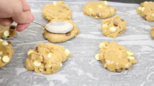 Scooping and Flattening Cookie Dough with White and Chocolate Chips onto A Parchment-Lined Baking Sheet