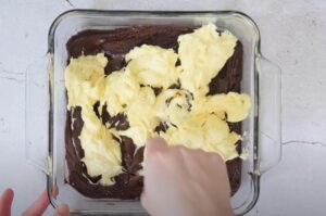 A layer of creamy yellow filling is being spread over a layer of fudgy brownies