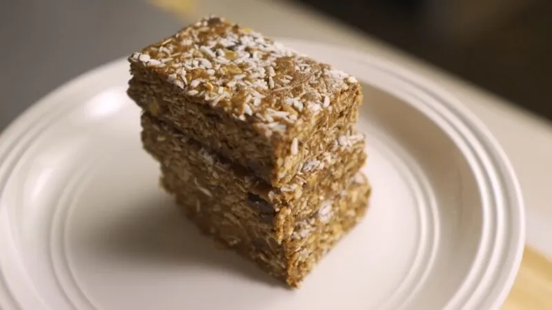 A Stack of Homemade Protein Bars Topped with Shredded Coconut Served on A White Plate