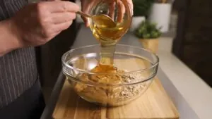 A Person Pouring Honey Into a Bowl of Almond Butter and Oats While Preparing Homemade Protein Bars