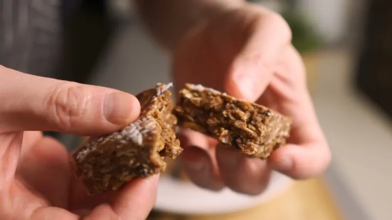 Hands Breaking Apart a Homemade Protein Bar Made with Wholesome Ingredients, Showcasing Its Chewy Texture