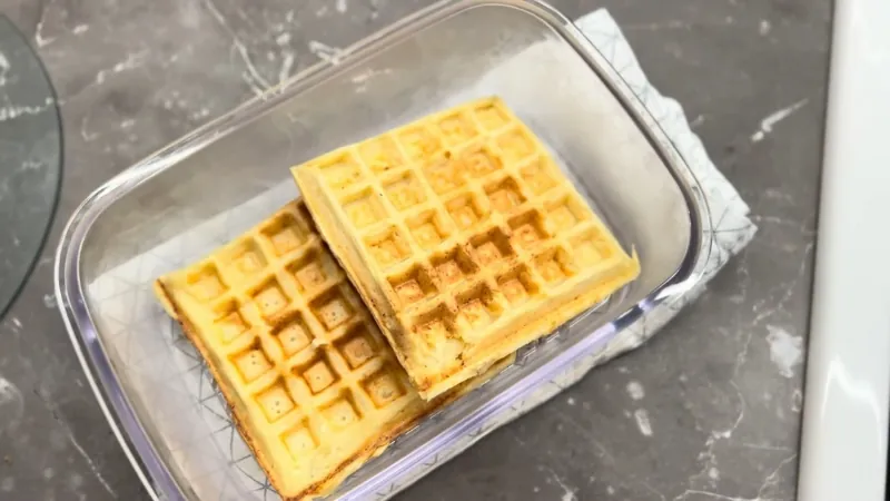 Two Golden-Brown Cottage Cheese Waffles in A Clear Glass Container on A Gray Countertop